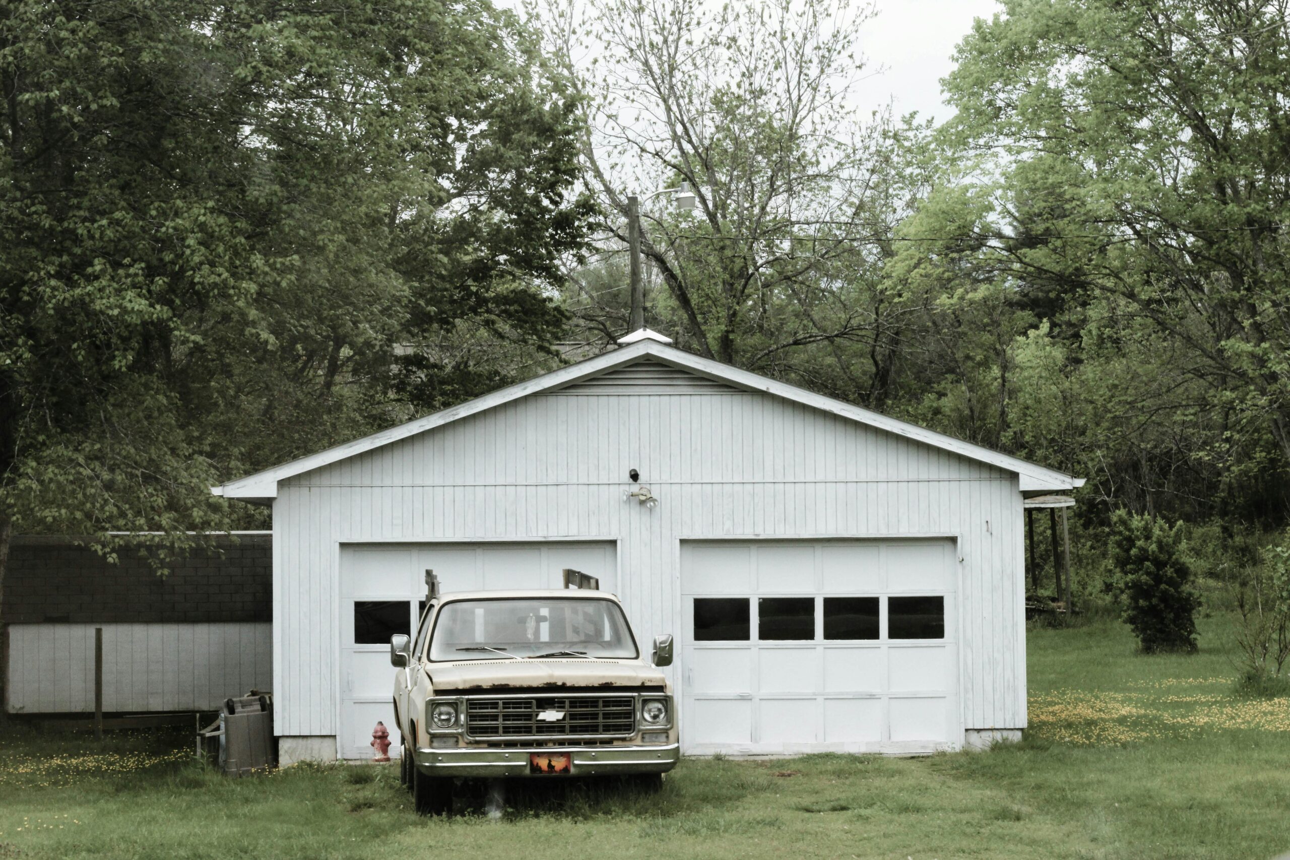 A classic pickup truck parked outside a wooden garage surrounded by lush greenery in Asheville, NC.